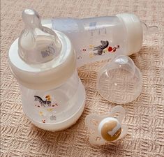 a baby bottle with its lid open next to an infant pacifier on the floor