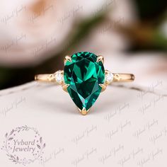 an emerald colored ring with three diamonds on it's sides, sitting on top of a white box