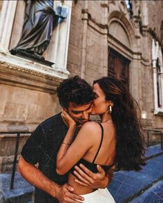 a man and woman kissing in front of a building with a statue on the side