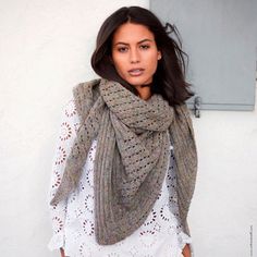 a woman wearing a gray scarf and white shirt is standing in front of a wall