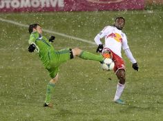 two men playing soccer in the rain on a field with snow falling all around them