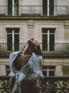 a woman leaning on a fence in front of a building and looking up at the sky