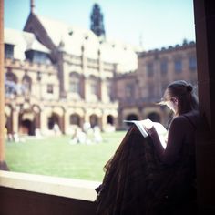 a woman sitting on a ledge reading a book