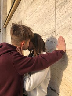 a man and woman kissing in front of a wall with their arms around each other