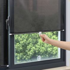 a person is holding something in their hand near a window with the blinds pulled down