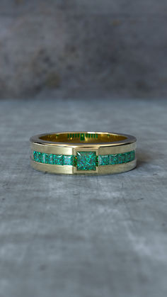 a yellow gold ring with green stones on the inside and outside, set against a gray background