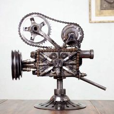 a metal object with gears attached to it on top of a wooden table next to a painting