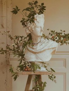 a white statue sitting on top of a wooden table covered in leaves and flowers next to a ladder