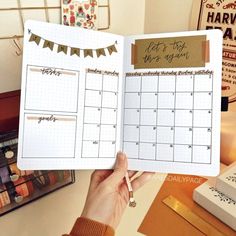 a person holding up a planner in front of a desk with other things on it