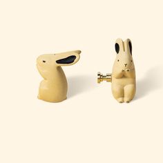 two small wooden rabbits with black eyes and ears, one is holding a brass faucet