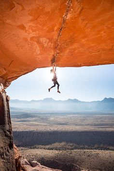 a man hanging from the side of a cliff with his feet in the air while rock climbing