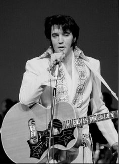 elvis presley singing into a microphone and holding an acoustic guitar