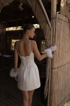 a woman in a short white dress is standing near a wooden structure and looking at something