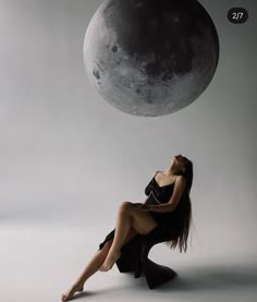 a woman sitting on the ground in front of a moon