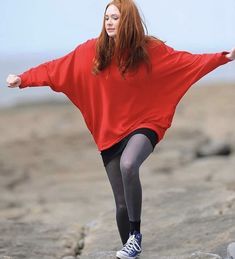 a woman in red shirt and black skirt standing on rocks with her arms spread out