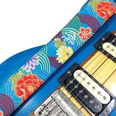 an electric guitar strap with flowers and leaves on it, sitting on top of a blue guitar