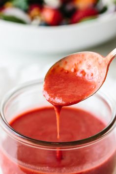 a spoon full of ketchup is being held over a jar filled with red sauce