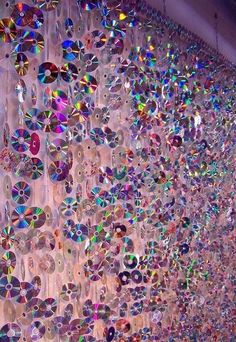 a wall covered with lots of different colored cds hanging from it's sides,