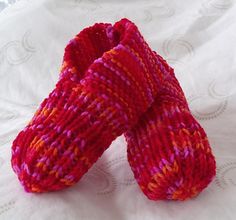 a pair of pink and orange knitted mittens on a white surface with circles