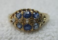 Quality early Edwardian 18ct solid gold diamond and sapphire gemstone ring. The head of the ring is marquise shaped, size 10.0mm{North to South} x 12.0mm{East to West} and is encrusted with rows of light blue sapphire gemstones and diamond gemstone chips. All of the gemstones are in top condition and exposed to the ring's reverse side to allow the light to shine through to make them glow, also for easy cleaning access. The shank is straight and displays a full striking Birmingham 18ct gold assay hallmark for the year 1903 on its inside circumference. Size 'R-S'{UK}, 9.25{US}. Weighs 3.1 grams. Superb condition throughout with genuine precious gemstones, no repairs and full authentication for its year of manufacture --- a pretty Edwardian example. Antique Sapphire Ring With 17 Jewels, Antique Blue Diamond Ring Hallmarked, Victorian Yellow Gold Diamond Ring With Gemstone, Victorian Sapphire Ring With Diamond Oval Shape, Victorian Oval Gemstone Diamond Ring, Victorian Oval Diamond Ring With Gemstone, Antique Sapphire Diamond Ring With Rose Cut, Victorian Oval Sapphire Ring With Diamond, Antique Oval Sapphire Ring With Single Cut Diamonds