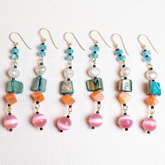 six pairs of earrings with different colored beads and pearls hanging from hooks on a white surface