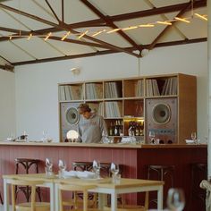 a woman behind the bar in a restaurant with lots of tables and chairs around it