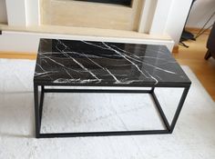 a black marble coffee table sitting on top of a white rug in front of a fireplace