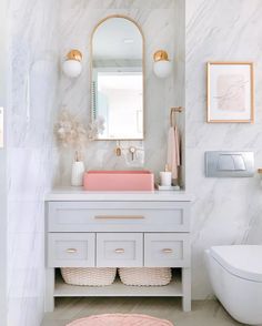 a white bathroom with marble walls and pink accents on the sink, toilet and mirror