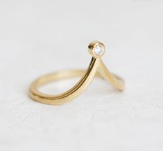 a gold ring with a single diamond on the top, sitting on a white surface