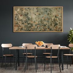 a dining room table with chairs and a large painting on the wall above it in front of a potted plant