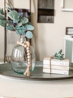 a glass vase filled with greenery sitting on top of a table next to two books