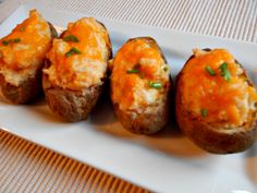 four baked potatoes with cheese and chives on a white plate