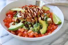 a white bowl filled with lots of different types of vegetables and avocado slices