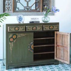 a green cabinet with flowers on it in front of a mirror and potted plant