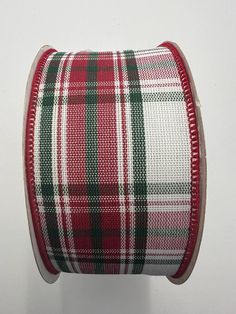 a spool of red and green plaid ribbon on a white surface with a black edge