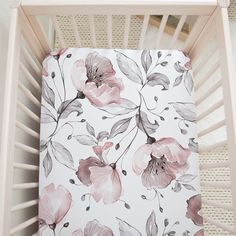 a white crib with pink flowers and leaves on the sheet in front of it