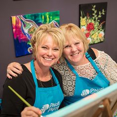 two women in aprons are smiling while painting