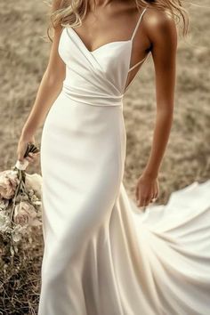 a woman in a white wedding dress standing on the grass with her hands behind her back