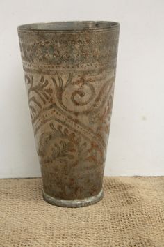 an old metal vase sitting on top of a burlocked cloth covered table