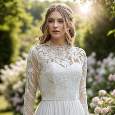 a woman wearing a wedding dress with sheer sleeves and lace on the top, standing in front of flowers