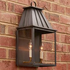 a wall mounted light with two candles on the front and side of it against a brick wall