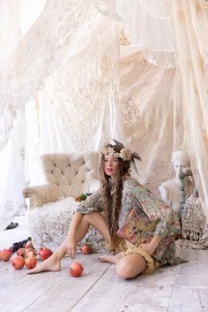 a woman with long hair sitting on the floor in front of some apples and other fruit