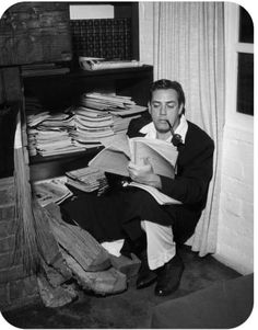 a man sitting on the floor reading a book in front of a pile of papers