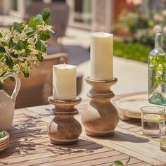 three candles sitting on top of a wooden table next to two vases and bottles