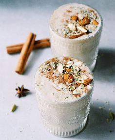 two cups filled with ice cream next to cinnamon sticks and star anise on the table