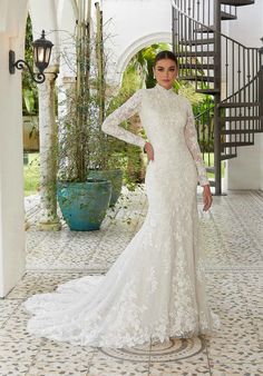 a woman in a long sleeved wedding dress standing on a tiled floor next to stairs