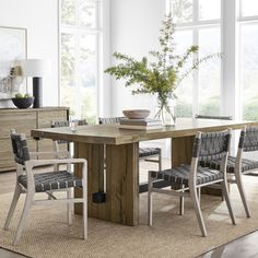 a dining room table with chairs and a vase on the table in front of large windows