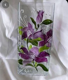 a glass vase with purple flowers painted on the side and green leaves in the middle