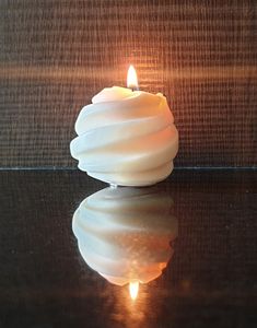 a white candle sitting on top of a table next to a glass surface with water