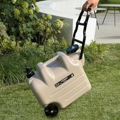 a hand is pulling a plastic water tank on wheels in the grass near a table and chairs